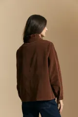 Camisa de pana color crema con cuello camisero con volados, cierre frontal de botones y mangas largas con puños abotonados. Presenta un bolsillo aplicado en el pecho y una silueta relajada.