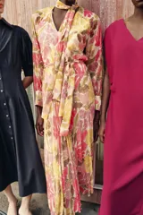 Vestido midi con estampado floral en tonos rosados, verdes y ocres. Presenta cuello con lazo, escote en pico, mangas largas con puños y cintura elástica con cinturón ajustable del mismo tejido. La falda cuenta con un diseño plisado y forro interior.