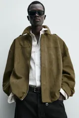 Cazadora cropped fit color verde militar, confeccionada en tejido efecto ante. Cuenta con cuello solapa, manga larga con puño abotonado, trabillas en los hombros, bolsillos laterales ocultos y un bolsillo interior. El bajo tiene elástico interior y el cierre frontal es con cremallera oculta por solapa con botones a presión.