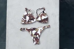 Conjunto de bikini con estampado de manchas tipo vaca en tonos marrones, blancos y verdes. El top es de estilo triangular con breteles regulables y cierre de gancho en la espalda. La bombacha es tipo vedetina con laterales fruncidos elásticos.