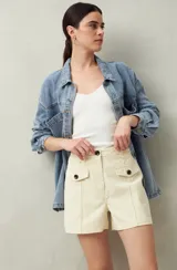 Short de tiro alto color beige, con bolsillos delanteros con solapa y botones a la vista.