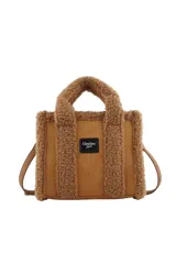 Cartera tipo tote bag de Las Oreiro, confeccionada en material tipo gamuza color beige con detalles de corderito sintético en los bordes y manijas. Incluye un parche frontal con el logo de la marca y correa ajustable extraíble.