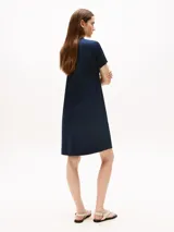 Vestido corto azul marino, tipo chomba, de corte evasé y manga corta. Presenta cuello en V con detalles en blanco y rojo, y logo bordado en la manga.