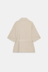 Chaqueta de estilo safari confeccionada en mezcla de lino, color azul marino, con cuello solapa, mangas cortas y cierre frontal con botones ocultos. Presenta bolsillos de parche en el pecho con solapa y botones, además de un cinturón ajustable del mismo tejido para anudar en la cintura.