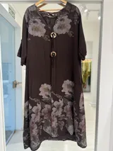 Vestido midi color marrón chocolate con estampa floral en tonos claros, escote en V y detalle de grandes botones circulares en el frente con tiras colgantes. Mangas cortas y corte holgado.