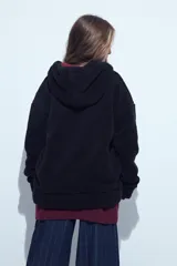 Canguro de corderito con capucha, cierre frontal y bolsillos laterales. Diseño relajado y textura suave.