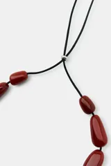 Collar de cordón negro con cuentas de resina en tonos rojizos y formas variadas, incluyendo una pieza central curva y un colgante grande en forma de gota.