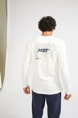 Remera de manga larga color mostaza, con cuello redondo y estampado frontal con las siglas MST en contorno verde.