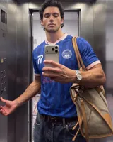 Camiseta de fútbol de manga corta en color azul con diseño estampado abstracto y cuello en V rosado con detalles blancos a juego con los puños. Presenta inscripciones y escudos deportivos en el pecho.