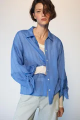 Camisa de cuello solapa y manga larga con detalle de lazos en los puños. Presenta un diseño de rayas verticales a tono y cierre frontal con botones ocultos.