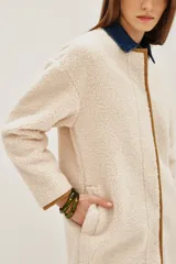 Saco de corte recto confeccionado en tejido tipo boucle color crema, con terminaciones en contraste color marrón y cierre frontal con botones metálicos.
