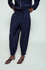 Pantalón de tiro alto de tela satinada color azul marino, con bolsillos frontales, cintura ajustable con cordones y puños elásticos en los tobillos.