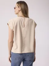 Blusa color beige de corte holgado, con cuello redondo y mangas cortas con dobladillo.