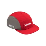 Gorro tipo cap de cinco paneles Supreme, confeccionado en tejido técnico GORE-TEX. Presenta una combinación de colores rojo y gris, con el logo de la marca bordado en un parche frontal y el logo de GORE-TEX estampado en el lateral.