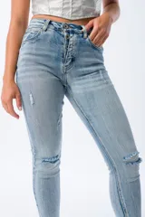 Pantalón de jean celeste claro, corte skinny, con roturas en las rodillas y muslos, tiro alto y cierre con botones.