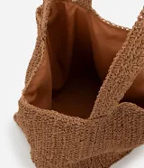 Bolso de playa tejido en fibra de papel color marrón claro, con asas medianas y detalle de logo metálico dorado en el centro.