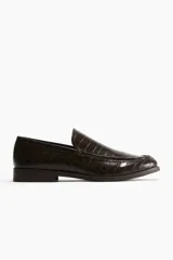 Mocasines de hombre en tejido revestido con textura efecto piel de cocodrilo en color marrón oscuro, con costura frontal tradicional y suela plana con pequeño tacón.
