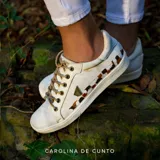 Championes de cuero color marfil de la marca Carolina De Cunto, con cordones tostados, suela de goma y detalles pintados a mano en el lateral con un aplique metálico triangular.