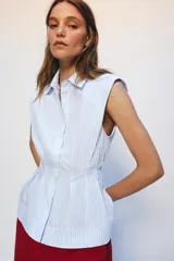 Camisa de algodón sin mangas con cuello solapa, diseño a rayas celestes y blancas, pliegues en la cintura y bajo evasé. Cierre frontal con botones ocultos.