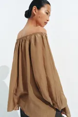 Blusa de lino color blanco, con escote recto ajustable mediante cordón y hombros descubiertos. Cuenta con manga larga abullonada terminada en elástico.