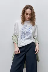 Remera negra de silueta amplia y calce relajado, con cuello redondo, mangas cortas con hombros caídos y estampa botánica en líneas blancas en el frente.