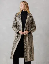 Trench de ecocuero con estampado animal print de serpiente en tonos beige, marrón y negro. Presenta cuello con solapa ancha, doble abotonadura frontal con botones negros, cinturón ajustable con hebilla metálica, mangas largas con presillas y botones en los puños, canesú suelto en la espalda, bolsillos laterales y forro interno.