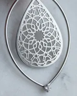 Caravanas de acero con diseño de gota calada, compuestas por una pieza triangular superior y un marco ovalado que contiene un patrón geométrico intrincado.