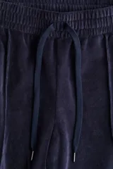 Pantalón tipo jogger de corte amplio confeccionado en tejido de velour suave. Presenta cintura elástica con cordón de ajuste y detalle de pliegue cosido vertical en el frente de cada pierna.