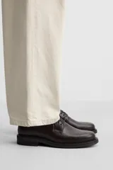 Zapato tipo blucher fabricado en piel de alta calidad, con cordonera de cinco pasados, horma redonda y suela a tono con ligero tacón.
