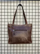 Cartera tipo tote de cuero vacuno negro con doble asa de hombro, panel superior liso y bolsillo exterior frontal con textura símil cocodrilo y costuras visibles en contraste.