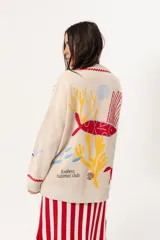 Saco oversize tejido con ilustraciones inspiradas en corales, peces, estrellas de mar y tortugas. Presenta galón picot en rojo en cartera y puños, y botones a tono.
