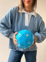 Buzo tipo chomba de corte oversize con diseño a rayas horizontales celestes y blancas. Presenta cuello camisero blanco y un bordado en la espalda con la inscripción República Oriental del Uruguay.