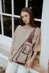 Bandolera de cuero color beige con detalles en bordó. Tiene correa ancha regulable para llevar cruzada al cuerpo, cierre principal con cremallera y dos bolsillos frontales con cierre.