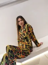 Conjunto de pijama de dos piezas con estampado floral y geométrico en tonos naranja, verde, amarillo y negro. Incluye camisa de manga larga con cuello y botones, y pantalón largo con cintura elástica.