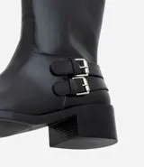Bota de caña corta marca Satinato, confeccionada en poliuretano color negro. Presenta punta redondeada, taco bloque bajo y dos tiras decorativas con hebillas metálicas en el lateral externo.