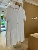 Vestido camisero blanco de lino fabricado en Italia, de manga corta, con botones de nácar y un volado en el ruedo final. Además, cuenta con un volado superior en un solo lado, creando un efecto irregular y con diseño.