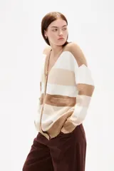 Saco de punto con diseño de rayas horizontales en tonos beige, crema y marrón. Presenta cuello en V, cierre frontal con botones y bolsillos laterales. De corte holgado y manga larga con puños acanalados.