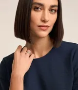 Blusa blanca de poliéster con cuello redondo, mangas cortas, cierre trasero en forma de gota, pequeñas aberturas laterales y acabados en pespuntes en las mangas y el cuello.