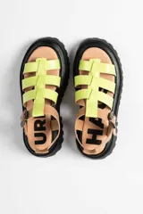 Sandalia tipo gladiadora con plataforma track negra. Presenta un diseño bicolor con tiras delanteras en color amarillo neón y talón con tira ajustable en color beige. Incluye hebilla metálica negra.