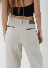 Pantalón sastrero de lino color gris claro melange, de tiro medio, con corte flojo que se afina suavemente hacia los tobillos. Cuenta con bolsillos frontales con detalles de pasamanería a rayas.