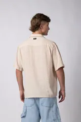 Camisa de hombre de manga corta color beige claro, confeccionada en lino. Tiene cuello clásico, cierre frontal con botones y corte recto.