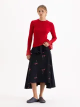 Top de tejido de punto fino color negro, con ajuste al cuerpo, cuello redondo y mangas largas que terminan en puños acampanados con detalle de tejido calado.