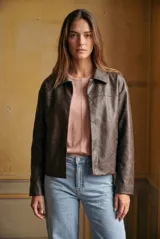 Campera de cuero vegano en tono marrón con acabado desgastado, corte recto y cierre frontal con botones a presión. Presenta cuello clásico y diseño minimalista.