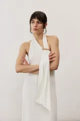 Vestido largo blanco de corte recto con escote halter y detalle de tiras drapeadas en el pecho sujetas con una hebilla metálica dorada.