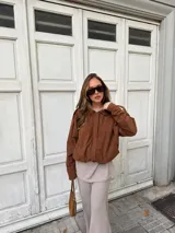 Campera de estilo bomber confeccionada en simil gamuza color marrón, con cuello camisero, cierre frontal oculto y puños elásticos.