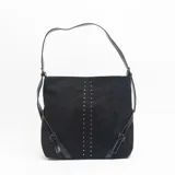 Cartera de hombro color negro, confeccionada en material tipo gamuza, con detalle de doble línea vertical de tachas metálicas en el frente y correas laterales ajustables con hebillas.