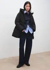 Campera puffer negra con capucha, diseño acolchado, cuello alto, bolsillos laterales con cierre y cierre frontal de cremallera doble.