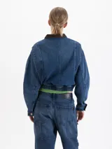 Campera bomber de denim azul con cierre frontal, cuello de pana en color marrón y bolsillos frontales con solapa. Presenta un diseño corto con cintura elástica.