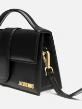 Bolso estructurado Jacquemus modelo Le Grand Bambino de cuero liso color negro, con asa superior, solapa frontal con cierre magnético, correa larga extraíble y logotipo metálico dorado.