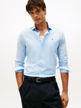 Camisa celeste de manga larga Tommy Hilfiger, confeccionada en algodón regenerativo, algodón BCI y elastano. Presenta cuello con contraste a color, cierre con botones y logo de la marca bordado en el pecho.